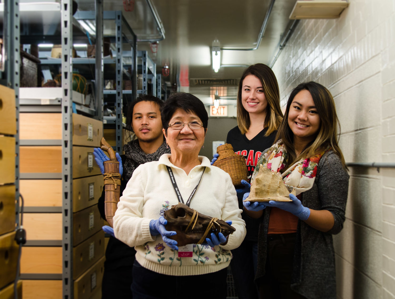 Image depicting volunteers Etta McKenna, Oscar Docto, Tess Madden, and Alpha Sadcopen posing with objects within CAS Mezzanine storeroom. Selected for use on the homepage of the Philippine Heritage Collections interactive web portal. (c) Field Museum of Natural History - CC BY-NC 4.0