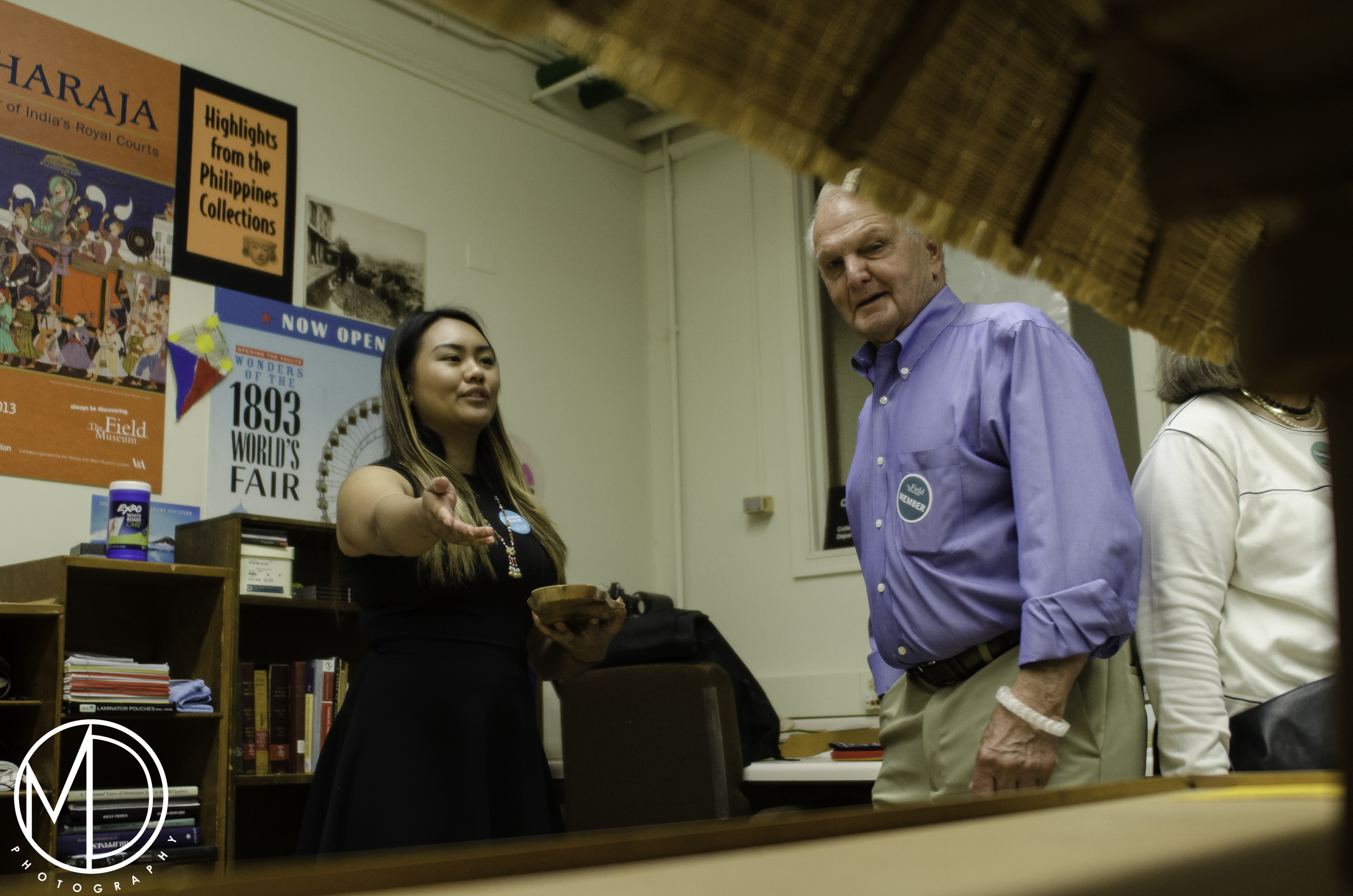 Alpha Sadcopen speaking to a guest and gesturing towards a replica of an Ifugao hut in the Philippines Collection. (c) Field Museum of Natural History - CC BY-NC 4.0