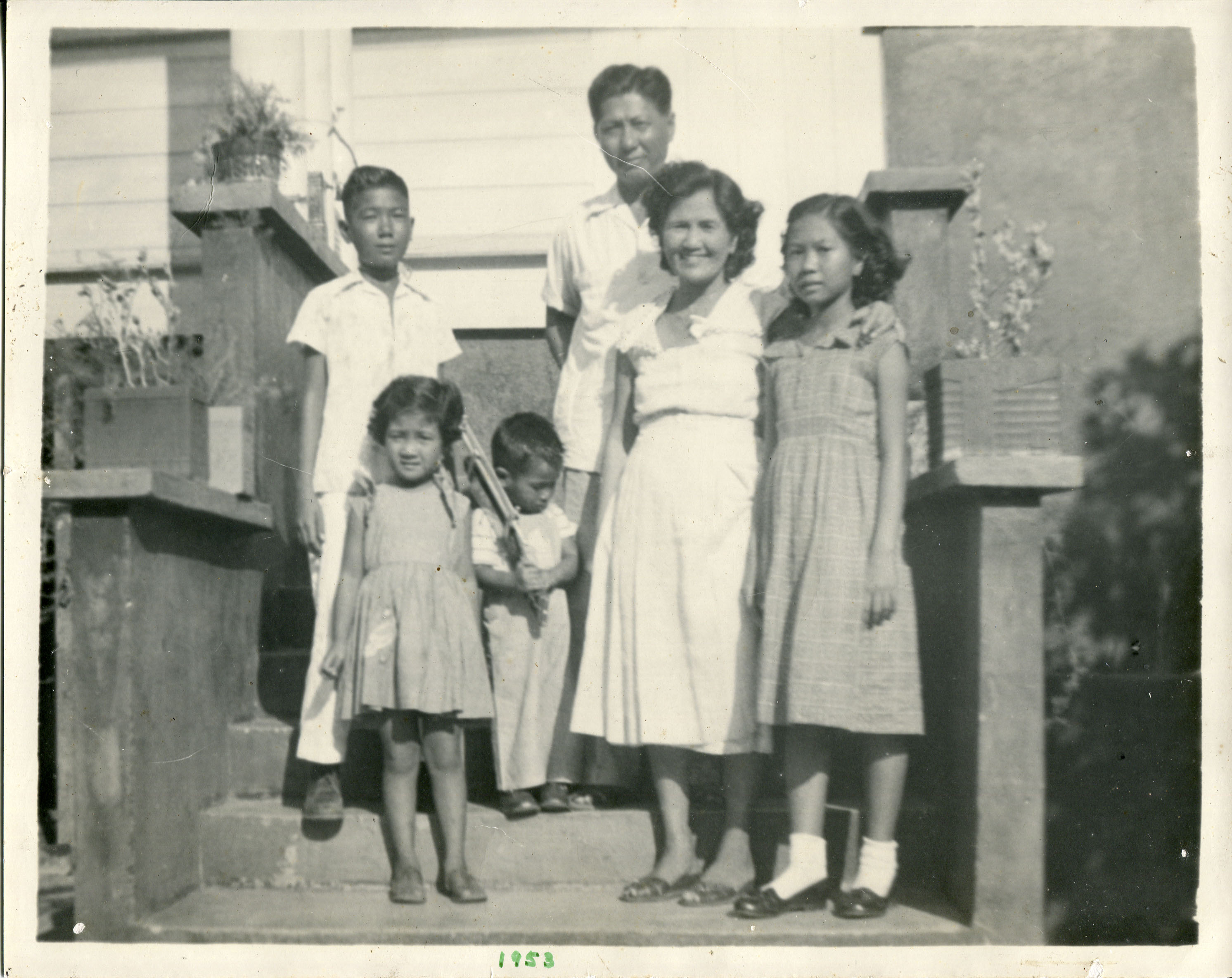 Family photo 1953 owned by Etta McKenna.1953 photo of family standing on the steps in front of our old house. Parents: Hermogenes Escarrilla (father) and mother Felicula Escarrilla. Brothers Efrain, Ernie. Sister EdnaNotes from Sarah Carlson, in discussion with McKenna: “Important to me because this is the only copy saved as all photos were destroyed due to termite infestation. That is why I want this digitized. Also makes me reminisce of all the things I did growing up in the house. Any views, findings, conclusions, or recommendations expressed in this story do not necessarily represent those of the National Endowment for the Humanities. (c) Field Museum of Natural History - CC BY-NC 4.0