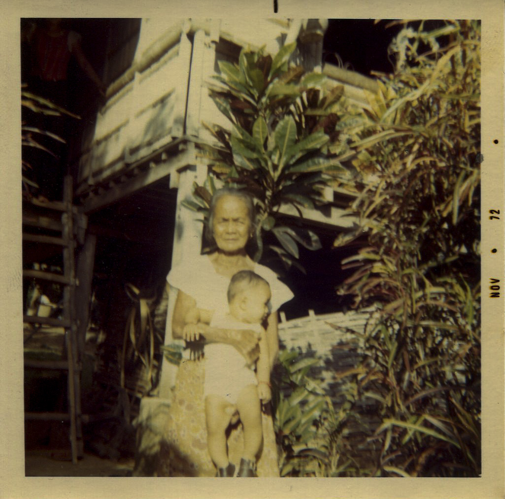Photo of Carnate's son and mother in-law, November 28, 1972Acquired from his wife. It was taken at his parent’s house in Tangcarang, Gerona, Tarlac.Pictured is Orlando Jr. and his maternal grandmother in front of their home. Orlando’s wife, Olivia Domingo [Carnate], was pregnant with Orlando Jr. when Orlando Sr. came to the US at age 28. His wife and son stayed behind for another 2 years before emigrating to join him. During this time that they were apart, his wife mailed him this photo.Written on photo: "Honey, little Orlando and Lola Petra. He is 9 months old. Love, Mommy Olivia Nov 28 ‘72." Any views, findings, conclusions, or recommendations expressed in this story do not necessarily represent those of the National Endowment for the Humanities. (c) Field Museum of Natural History - CC BY-NC 4.0