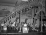 School children and fossils in Hall 38, tail of Brontosaurus skeleton. For Raymond Foundation. Charles R. Knight murals in the background.