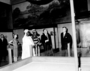 Sultan Seidou Njoya Njimouluh and Queen Ramatou Ngamdomboue, tribal rulers from Cameroon, Africa touring Museum with Lee Webber, standing in Hall 38 near Charles Knight murals.