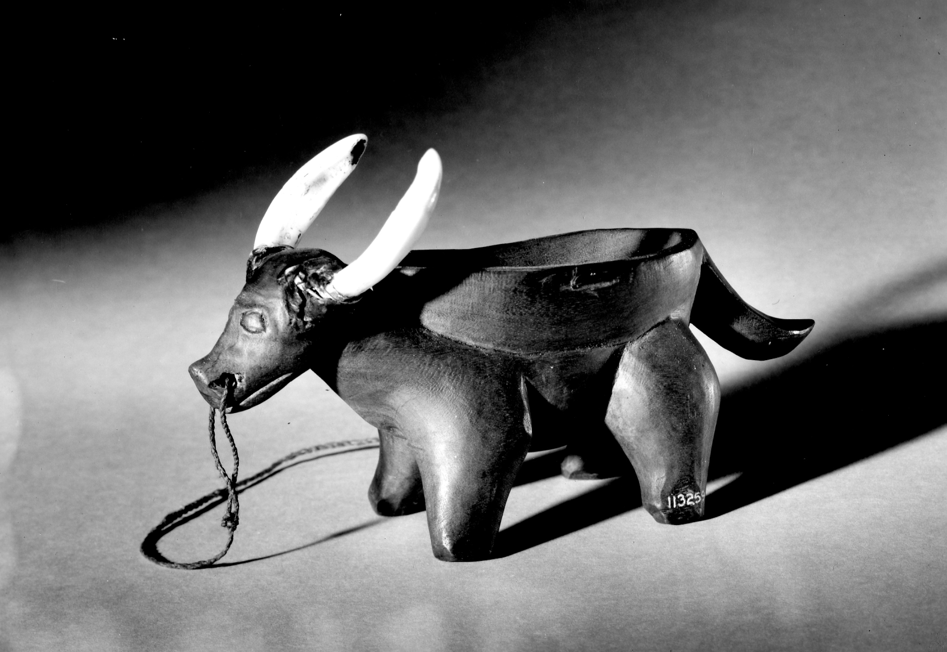 Bowl of light wood; rests upon carved caribou-like animal figure. Hog teeth for horns  