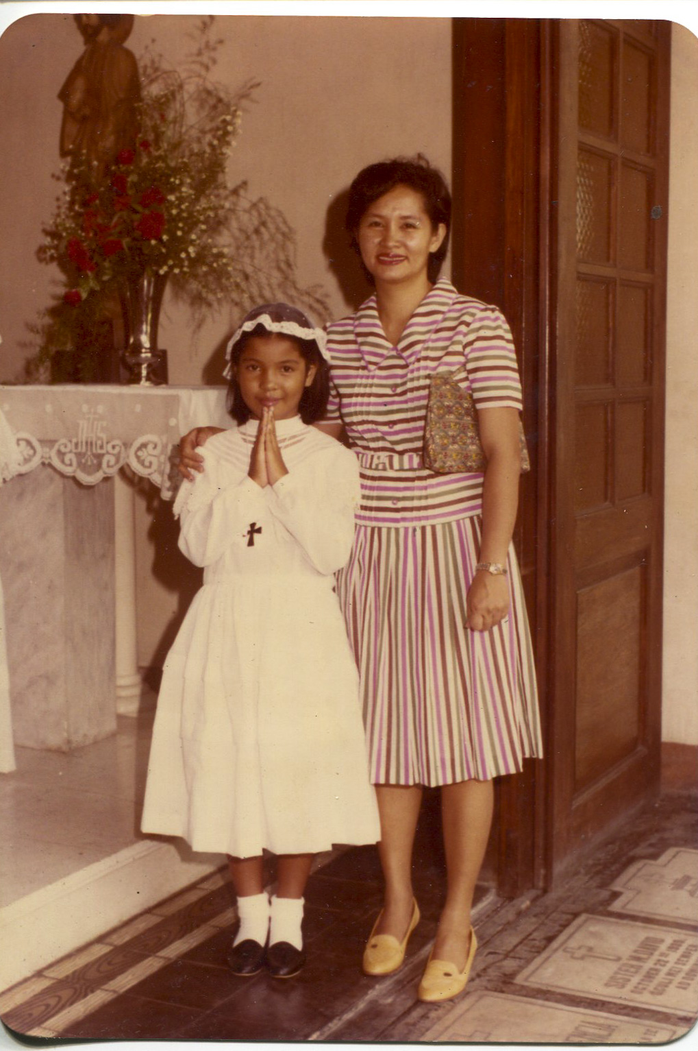 Photo of Escarilla-Carnate and mother, 1982Escarilla-Carnate said, “Taken in February or March 1982 by a professional photographer when I was in 2nd grade at Assumption School in Iloilo City. It was in a family album. Pictured are my mother and me. My catholic faith is important and I continue to practiceCatholicism here in the USA. My son has already had his first communion.” Any views, findings, conclusions, or recommendations expressed in this story do not necessarily represent those of the National Endowment for the Humanities. 