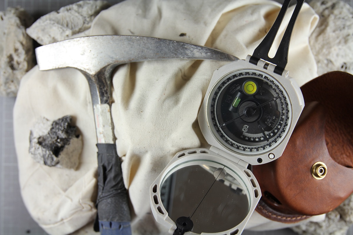 Basic tools of a geologist rock hammer, sample bag, and Brunton compass.